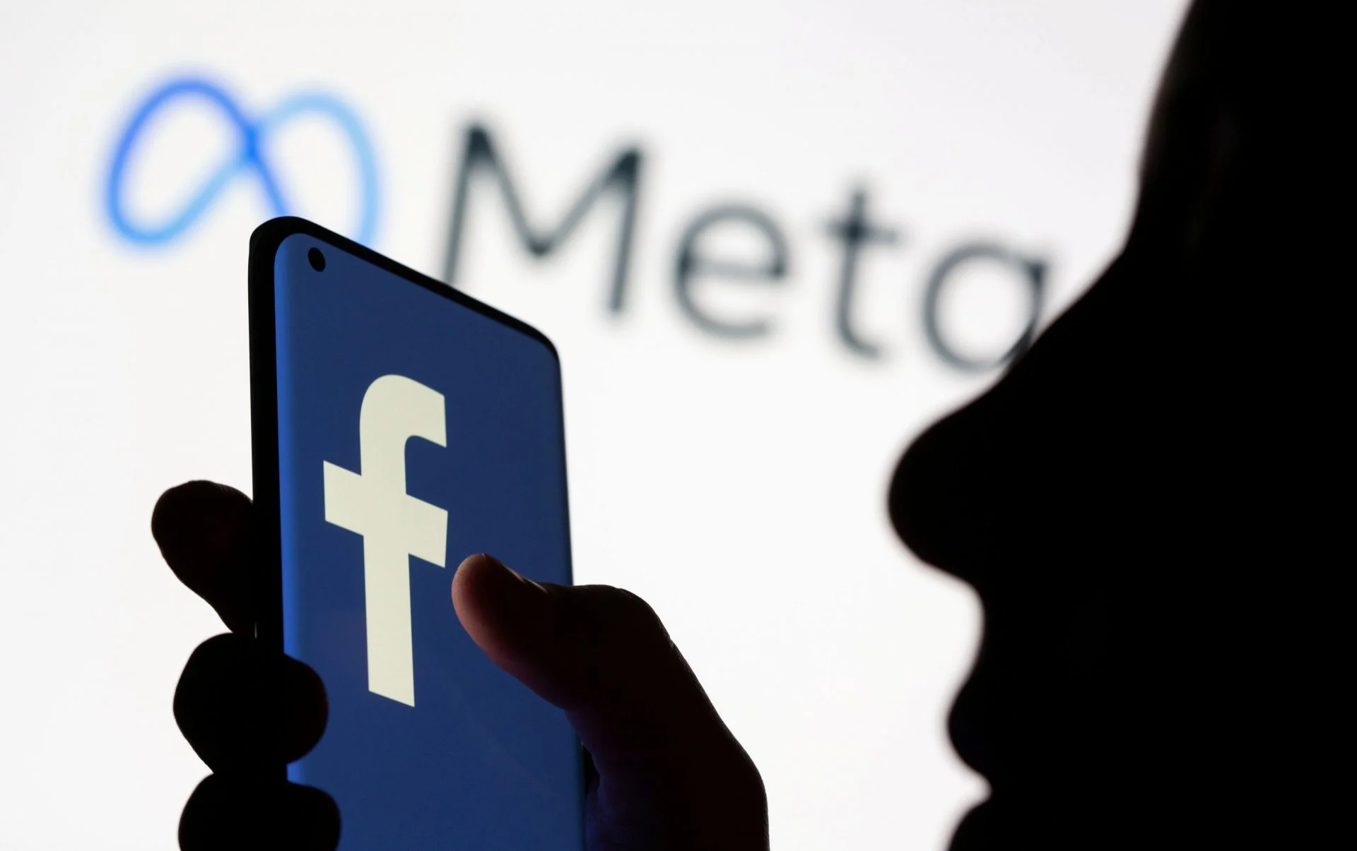 FILE PHOTO: Woman holds smartphone with Facebook logo in front of a displayed Facebook's new rebrand logo Meta in this illustration picture meta, facebook,